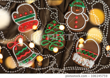 Banner for Christmas and New Year gingerbread. Christmas trees, toys, snowmen, garlands on a background of brown silk fabric. Bright bokeh. Banner for Christmas and New Year gingerbread. Christmas trees, toys, snowmen, garlands on a background of brown silk fabric. Bright bokeh. 106145759