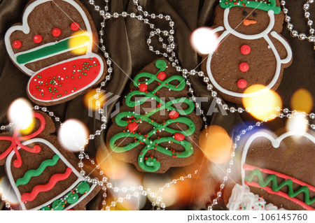 Banner for Christmas and New Year gingerbread. Christmas trees, toys, snowmen, garlands on a background of brown silk fabric. Bright bokeh. Banner for Christmas and New Year gingerbread. Christmas trees, toys, snowmen, garlands on a background of brown silk fabric. Bright bokeh. 106145760