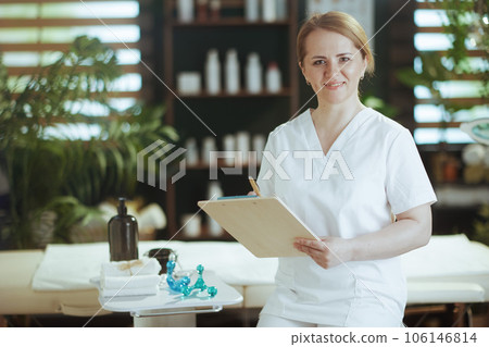 happy massage therapist woman in massage cabinet with clipboard 106146814