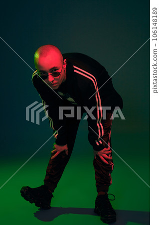 Studio shot of a young tattoed bald man posing against a colorful background. 90s style. Studio shot of a young tattoed bald man posing against a colorful background. 90s style. 106148189