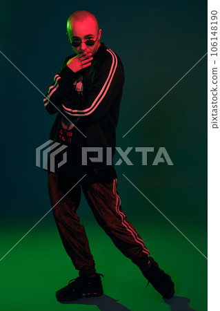 Studio shot of a young tattoed bald man posing against a colorful background. 90s style. Studio shot of a young tattoed bald man posing against a colorful background. 90s style. 106148190
