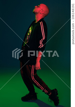 Studio shot of a young tattoed bald man posing against a colorful background. 90s style. Studio shot of a young tattoed bald man posing against a colorful background. 90s style. 106148191