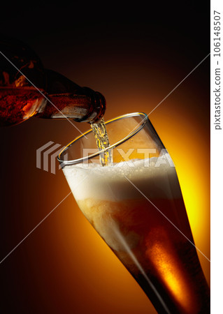 Pouring beer into a tall glass. 106148507