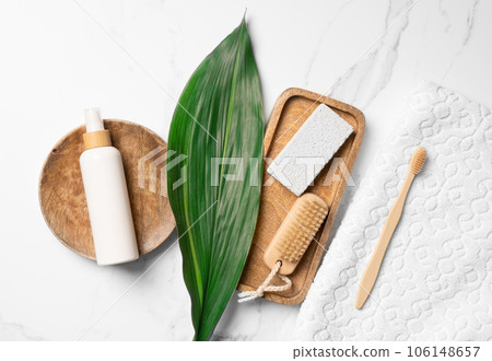 Flat lay of body care essentials including a toothbrush, white towel, pumice stone, brush, green leaf, and cosmetic bottle mockup in white. Flat lay of body care essentials including a toothbrush, white towel, pumice stone, brush, green leaf, and cosmetic bottle mockup in white. 106148657
