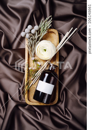 Scented home perfume in glass jar with rattan sticks on wooden tray, luxury aroma oil with woody and flowers fragrance concept. Scented home perfume in glass jar with rattan sticks on wooden tray, luxury aroma oil with woody and flowers fragrance concept. 106148661