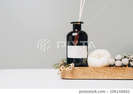 Scented home perfume in glass jar with rattan sticks on wooden tray, luxury aroma oil with woody and flowers fragrance. Scented home perfume in glass jar with rattan sticks on wooden tray, luxury aroma oil with woody and flowers fragrance. 106148662