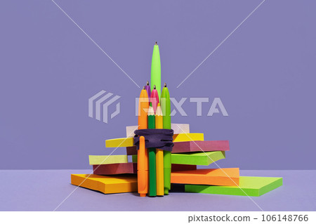 Stationery rocket out of pens on desk on top of pile of sticky notes. purple background. back to school or education and creativity concept. Success achievement. Team work ideas and leadership Stationery rocket out of pens on desk on top of pile of sticky notes. purple background. back to school or education and creativity concept. Success achievement. Team work ideas and leadership 106148766