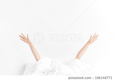 Early morning wake up with female hands from blanket. Woman lying in cozy white linen. Background with copy space. Early morning wake up with female hands from blanket. Woman lying in cozy white linen. Background with copy space. 106148771