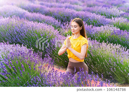 Yoga in lavender field. Young woman practicing yoga meditatation together with aromatherapy behind blooming lavender flowers. Early morning atmosphere. 106148786