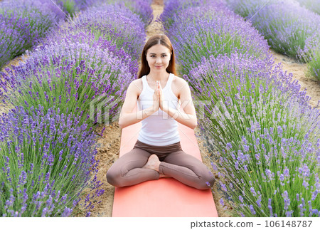 Yoga in lavender field. Young woman practicing yoga meditatation together with aromatherapy behind blooming lavender flowers. Early morning atmosphere. 106148787