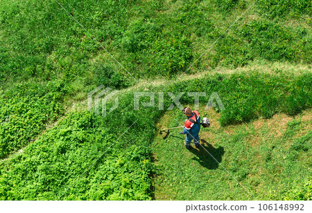 Weed control with grass mowing. Employee mows overgrown grass with a lawnmower. Aerial view from above. Weed control with grass mowing. Employee mows overgrown grass with a lawnmower. Aerial view from above. 106148992