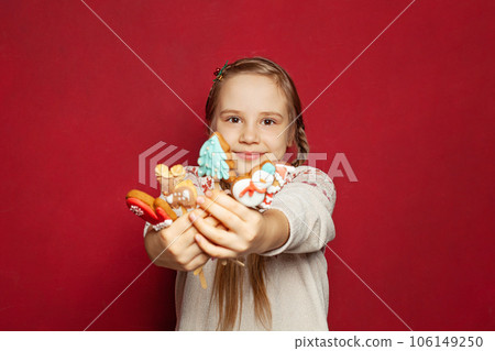 Cute little girl with pigtails showing Xmas cookies on red background, winter portrait 106149250