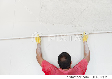 Plasterer levels the walls with gypsum plaster using an aluminum plaster rule after machine application. 106149945