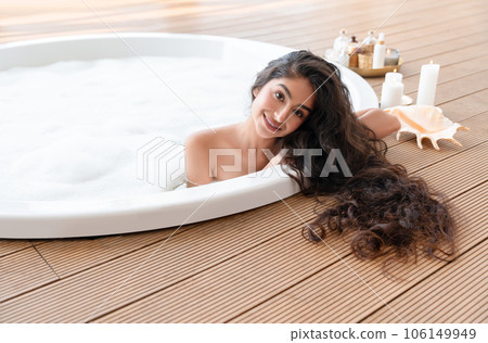 Beautiful Indian girl with long hair taking round bubble bath built in terrace board flooring. Comfortable house or apartment, interior design, resort and spa background. 106149949
