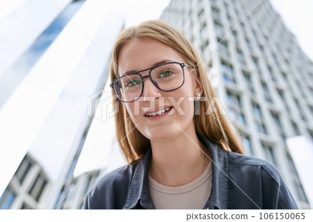 Teenage female in glasses looking at camera, glass skyscrapers background 106150065