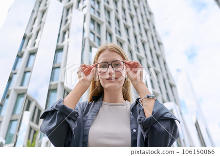 Teenage female in glasses looking at camera, glass skyscrapers background Teenage female in glasses looking at camera, glass skyscrapers background 106150066