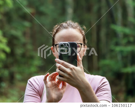 Berlin, Germany July 15 2023 Woman covering face with mobile phone, taking photo in nature 106150117