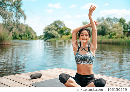 Indian woman doing yoga by the river on a pier Indian woman doing yoga by the river on a pier 106150259