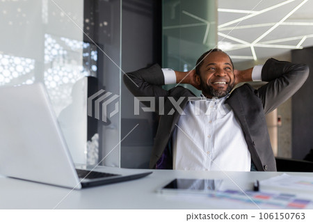 Well done businessman successfully completed the work, rests in the office dreamily and thoughtfully, the man throws his hands behind his head and visualizes the future victories and achievement. 106150763