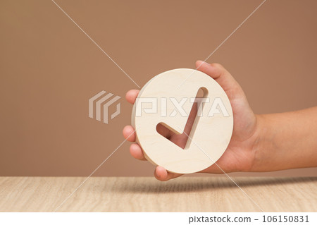 Hand holding check mark icon, banner with wooden check mark icon in hand, right sign. On a brown background. Copy space. Place for text 106150831
