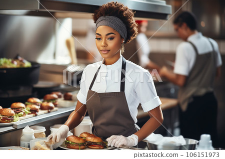 African american chef woman preparing burgers in a professional kitchen.  106151973