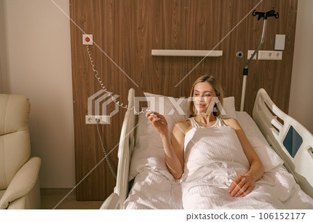 Young smiling woman patient holding emergency call button while lying in hospital bed 106152177