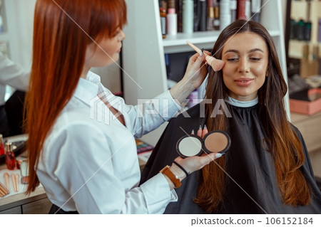 Professional makeup artist applying bronzer powder with a brush in beauty salon 106152184