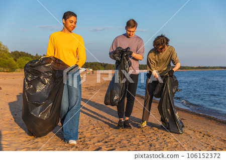 Earth day. Volunteers activists collects garbage cleaning of beach coastal zone. Woman mans with trash in garbage bag on ocean shore. Environmental conservation coastal zone cleaning. Blurred video 106152372