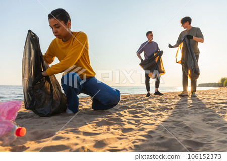 Earth day. Volunteers activists collects garbage cleaning of beach coastal zone. Woman and mans puts plastic trash in garbage bag on ocean shore. Environmental conservation coastal zone cleaning 106152373
