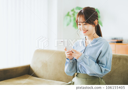 Woman sitting on a sofa and looking at a smartphone 106155405