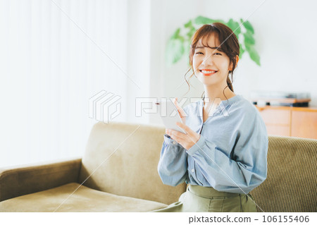 Woman sitting on the couch and holding a smartphone 106155406