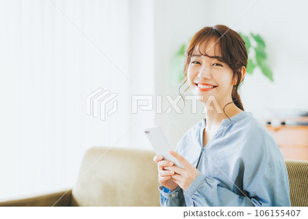 Woman sitting on the couch and holding a smartphone Woman sitting on the couch and holding a smartphone 106155407