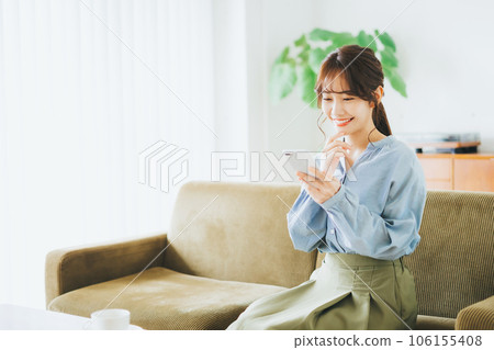 Woman sitting on a sofa and looking at a smartphone Woman sitting on a sofa and looking at a smartphone 106155408