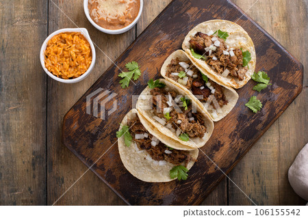 Pork carnitas tacos with onion and cilantro served with rice and refried beans Pork carnitas tacos with onion and cilantro served with rice and refried beans 106155542