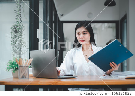 Business woman in white shirt using laptop computer and sitting by the table in office.. Business woman in white shirt using laptop computer and sitting by the table in office.. 106155922