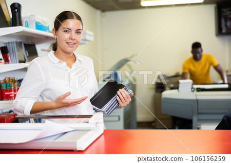 Cheerful young woman in white shirt smiling at the camera and holding new planners in the printing house 106156259