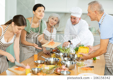 Pleased middle-aged woman attendee of cooking course demonstrating piece of salmon on cutting board 106156342