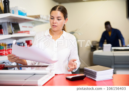 Focused young female typographer trimming the printed work on the cutter in the typography 106156403