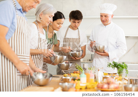 Cheerful middle-aged man chef of cooking course teaching attendees how to mix sauce 106156454