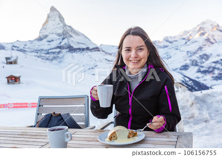 Happy traveler woman drinking mulled wine with strudel against snow covered mountains Happy traveler woman drinking mulled wine with strudel against snow covered mountains 106156755