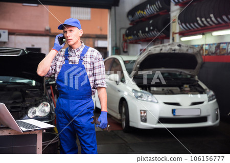 Confident auto mechanic talking on a smartphone in car service Confident auto mechanic talking on a smartphone in car service 106156777