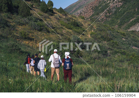 group of people tourists travelers with backpacks on hike in field in the mountains in nature in summer group of people tourists travelers with backpacks on hike in field in the mountains in nature in summer 106159904