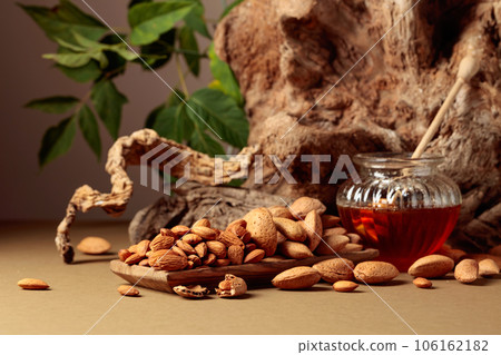 Almond nuts in a wooden dish and honey in a glass jar. 106162182