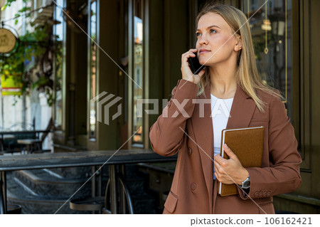 Business woman with notepad in hand speaks on the phone outdoors Business woman with notepad in hand speaks on the phone outdoors 106162421