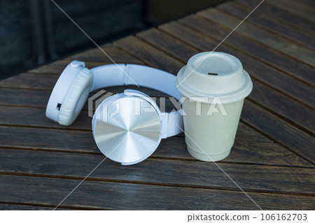 Paper cup and headphones on wooden table outdoors Paper cup and headphones on wooden table outdoors 106162703