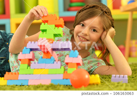 Portrait of cute girl playing with colorful plastic blocks in room 106163063