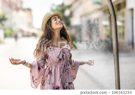 A beautiful young woman cools down under a water gate on a hot summer day 106163254