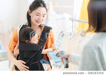 A young mother holding a baby shopping while operating a smartphone in a shopping mall 106163358