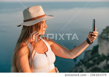 Selfie woman in hat, white tank top and shorts makes selfie shot mobile phone post photo social network outdoors on sea background beach people vacation lifestyle travel concept. 106163379