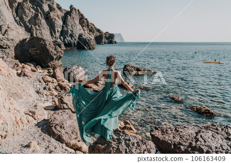 Woman green dress sea. Woman in a long mint dress posing on a beach with rocks on sunny day. Girl on the nature on blue sky background. 106163409